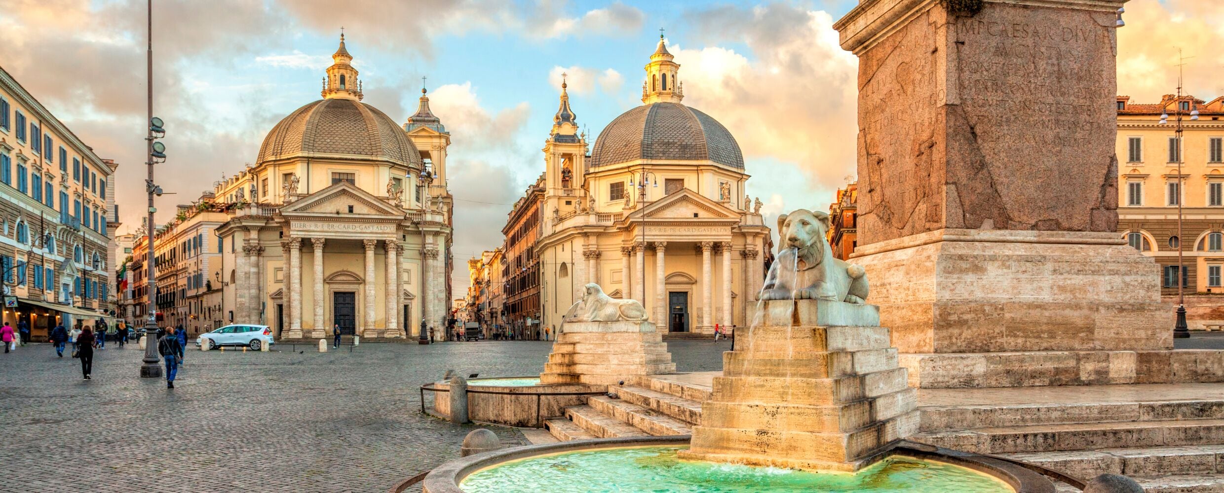 A historic square with classical architecture, including domed buildings and a fountain.