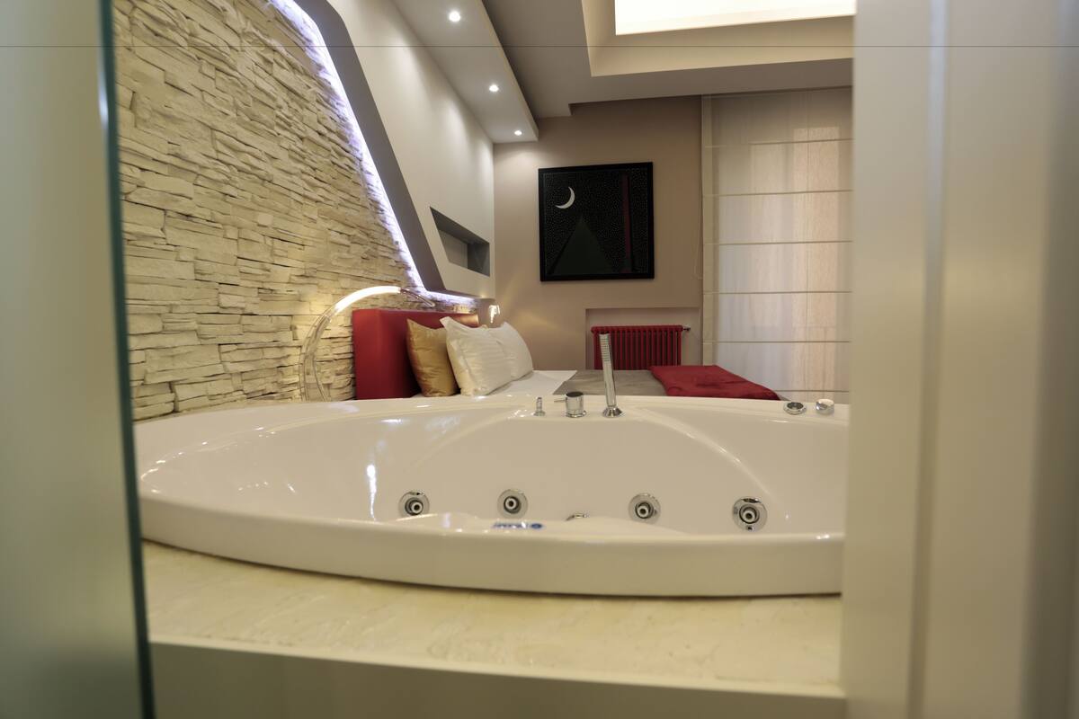 A modern bathroom with a large bathtub, a stone wall, and a painting of a crescent moon.