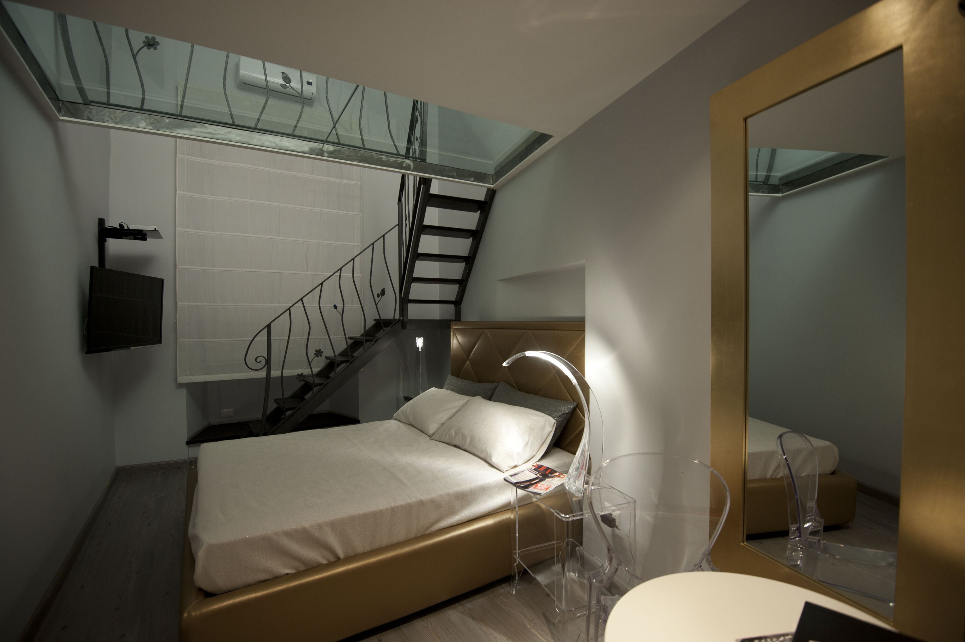 Un dormitorio moderno con cama, mesita de noche, espejo y una escalera.