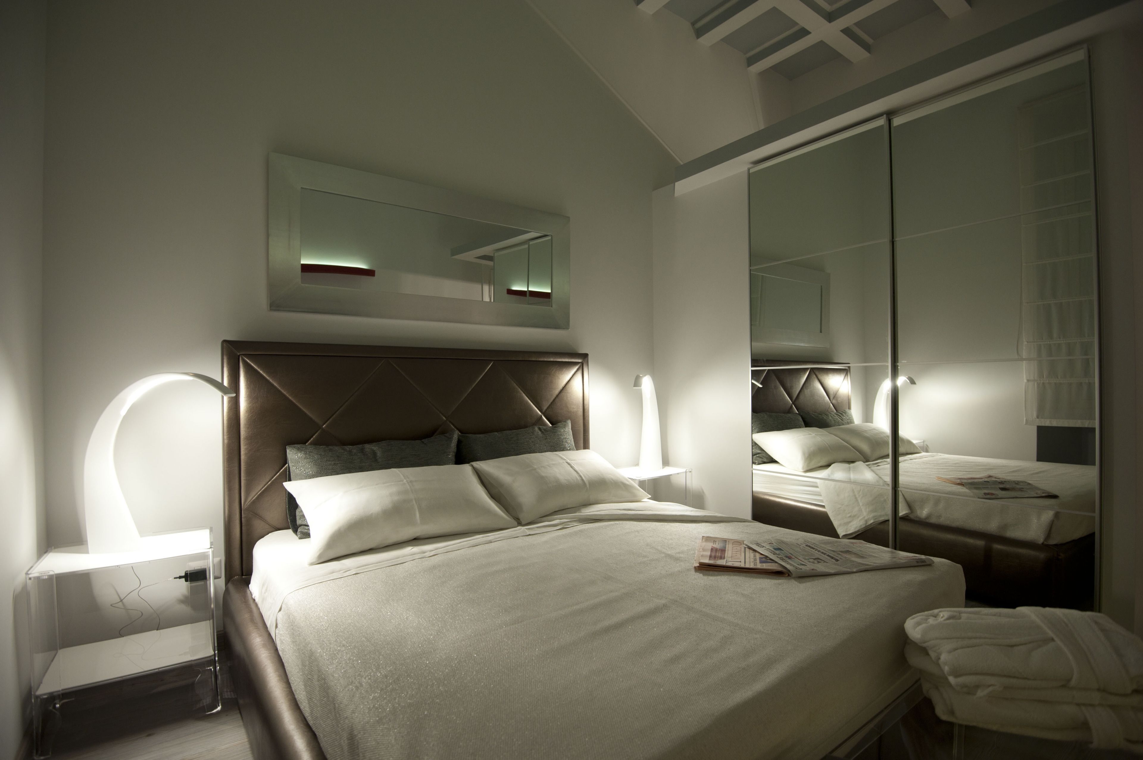 A modern hotel room with a large bed, bedside lamps, a mirror, and a wardrobe.