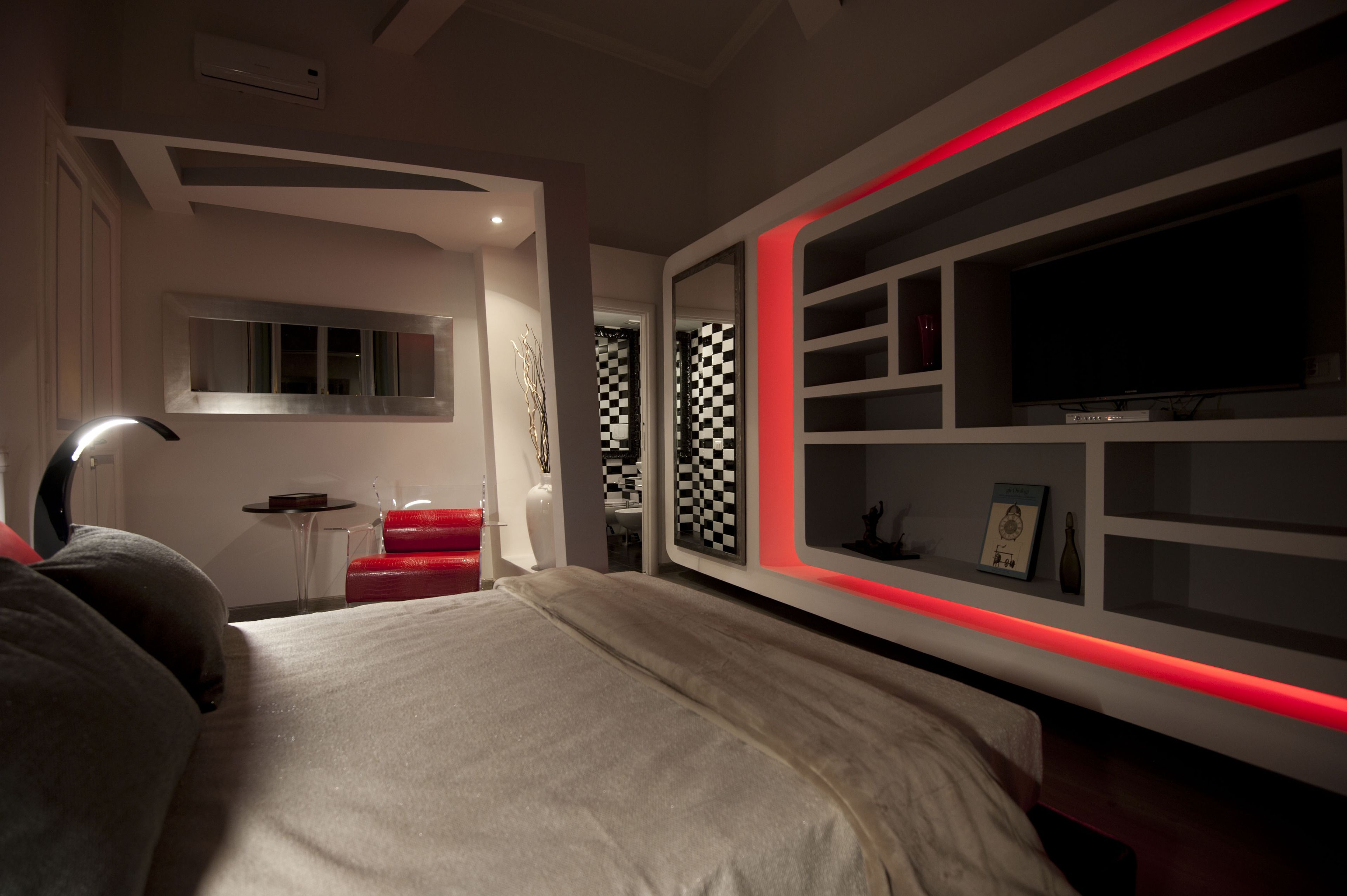 Een moderne slaapkamer met een groot bed, een aan de muur bevestigde televisie en een rode lichtstrip.