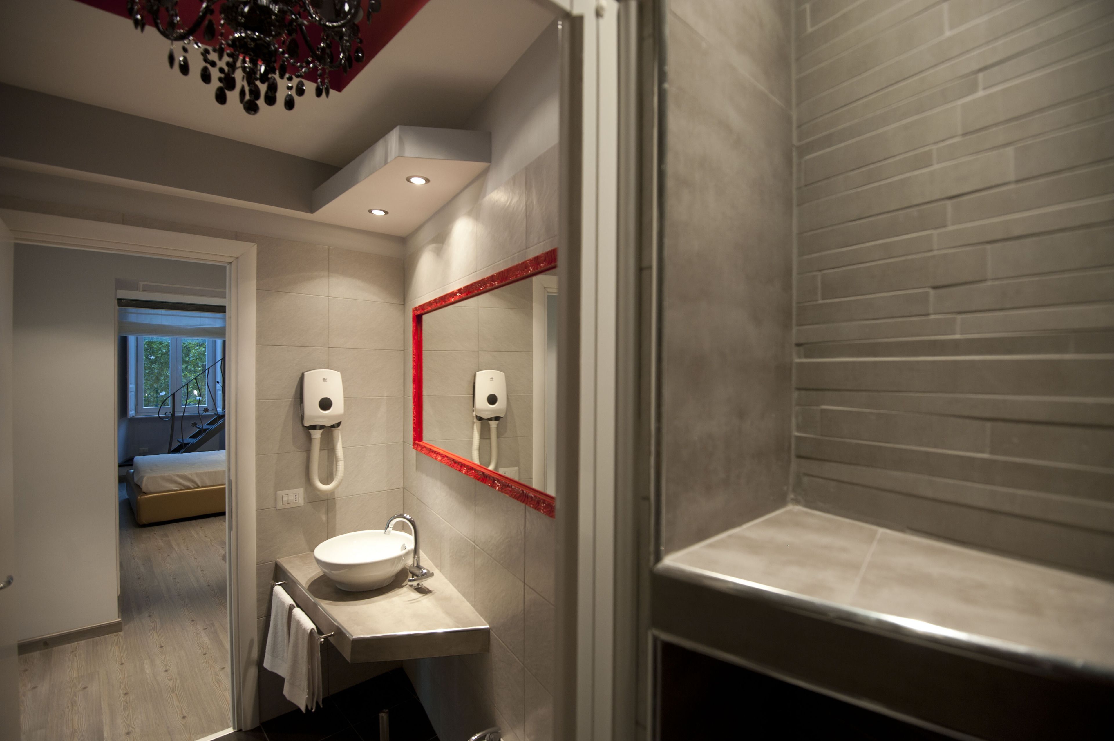 Un bagno moderno con un lavandino bianco, uno specchio con cornice rossa e una zona doccia.