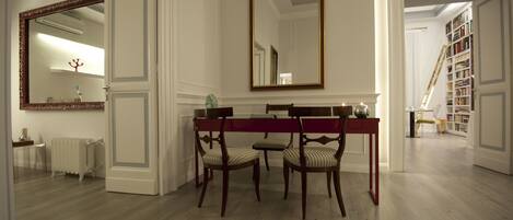 A dining area with a wooden table and chairs, a large mirror, and a bookshelf in the background.