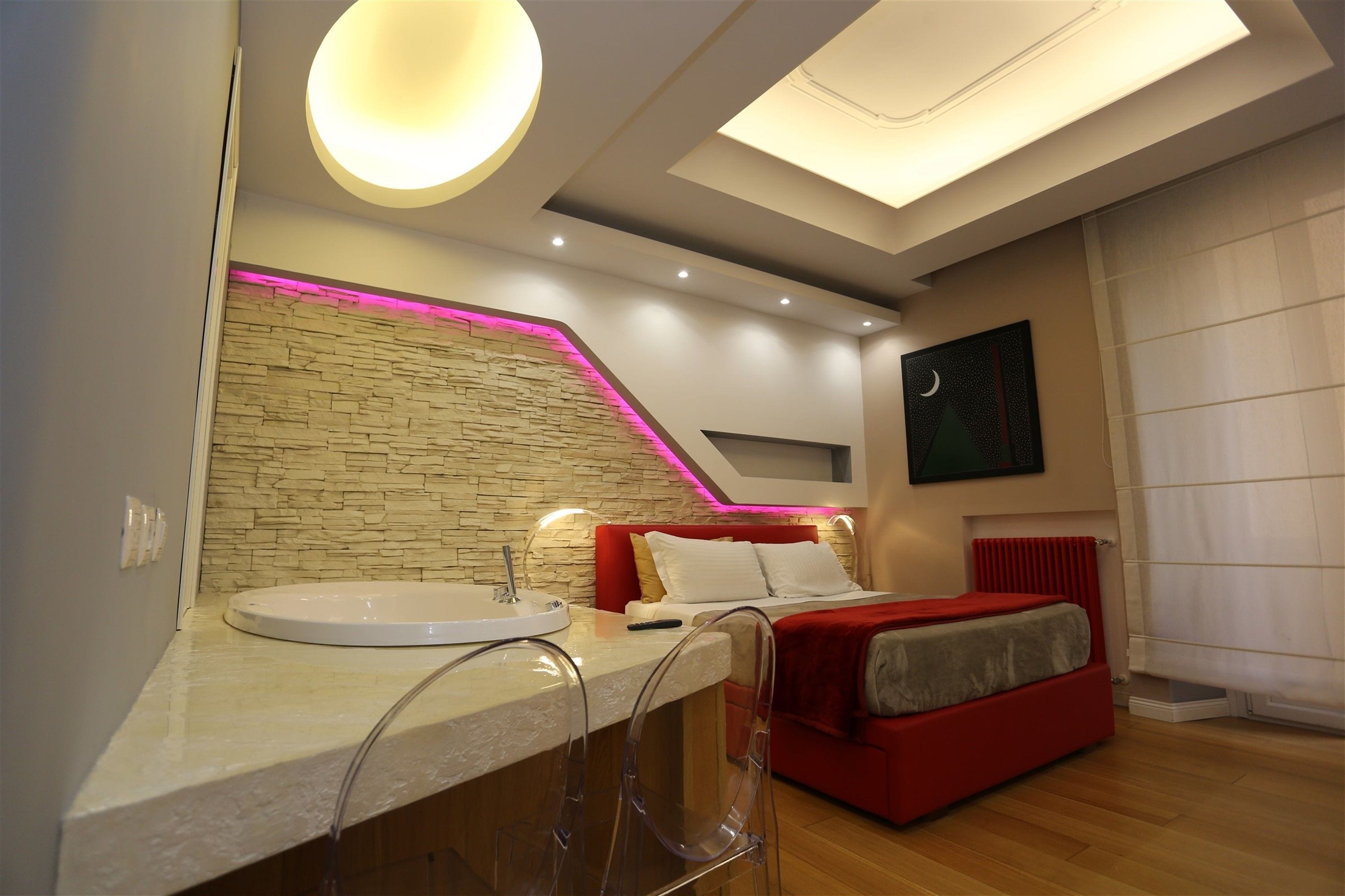Ein modernes Schlafzimmer mit einer Wand aus Stein, einer runden Deckenleuchte, einem Bett mit roter Bettwäsche und einem weißen Heizkörper.