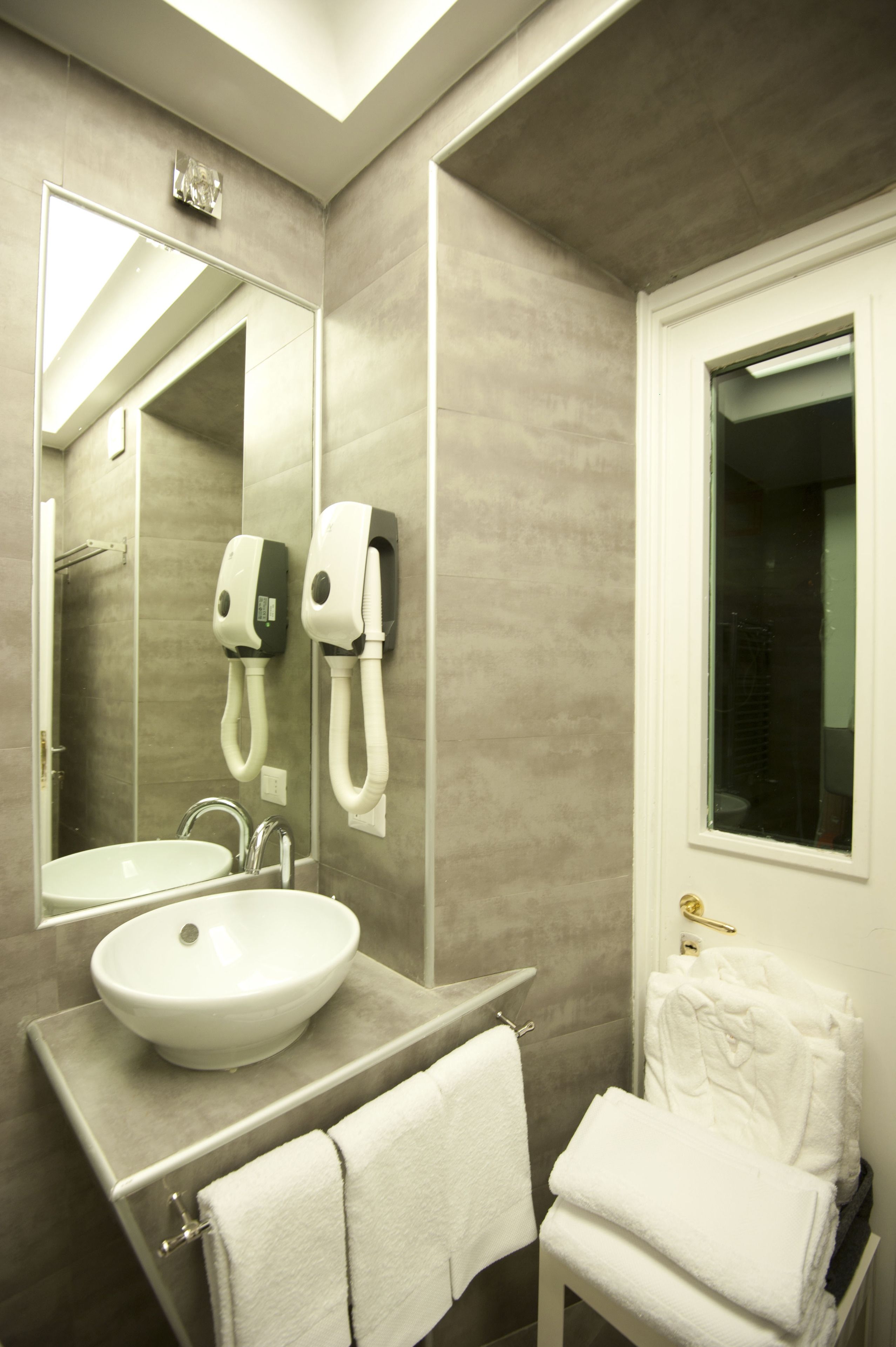 Un baño moderno con un espejo grande, un lavamanos, toalleros y una ventana.