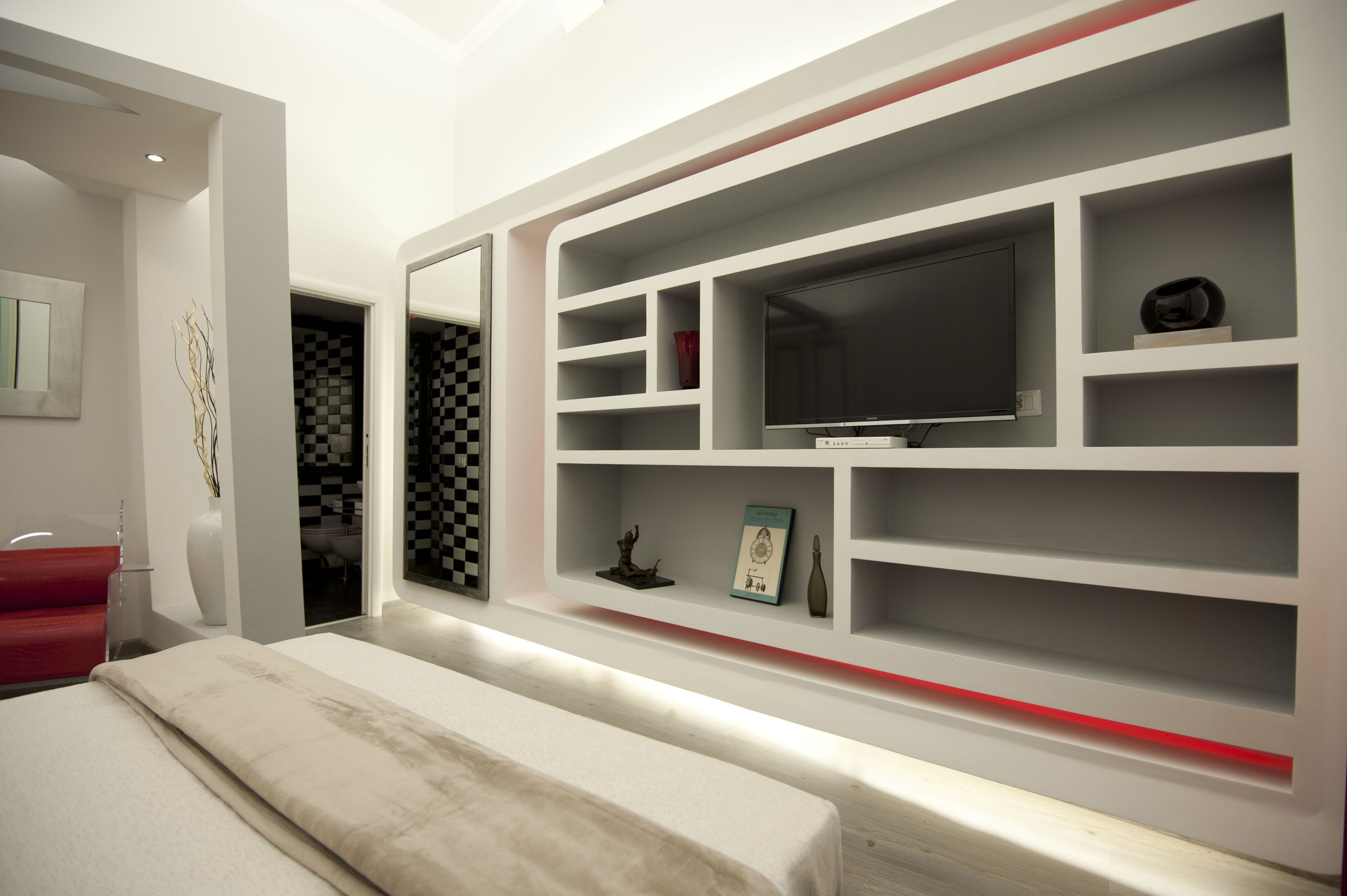 Quarto moderno com uma cama grande, televisão e estantes embutidas com diversos objetos.