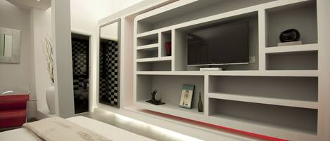 Quarto moderno com uma cama grande, televisão e estantes embutidas com diversos objetos.