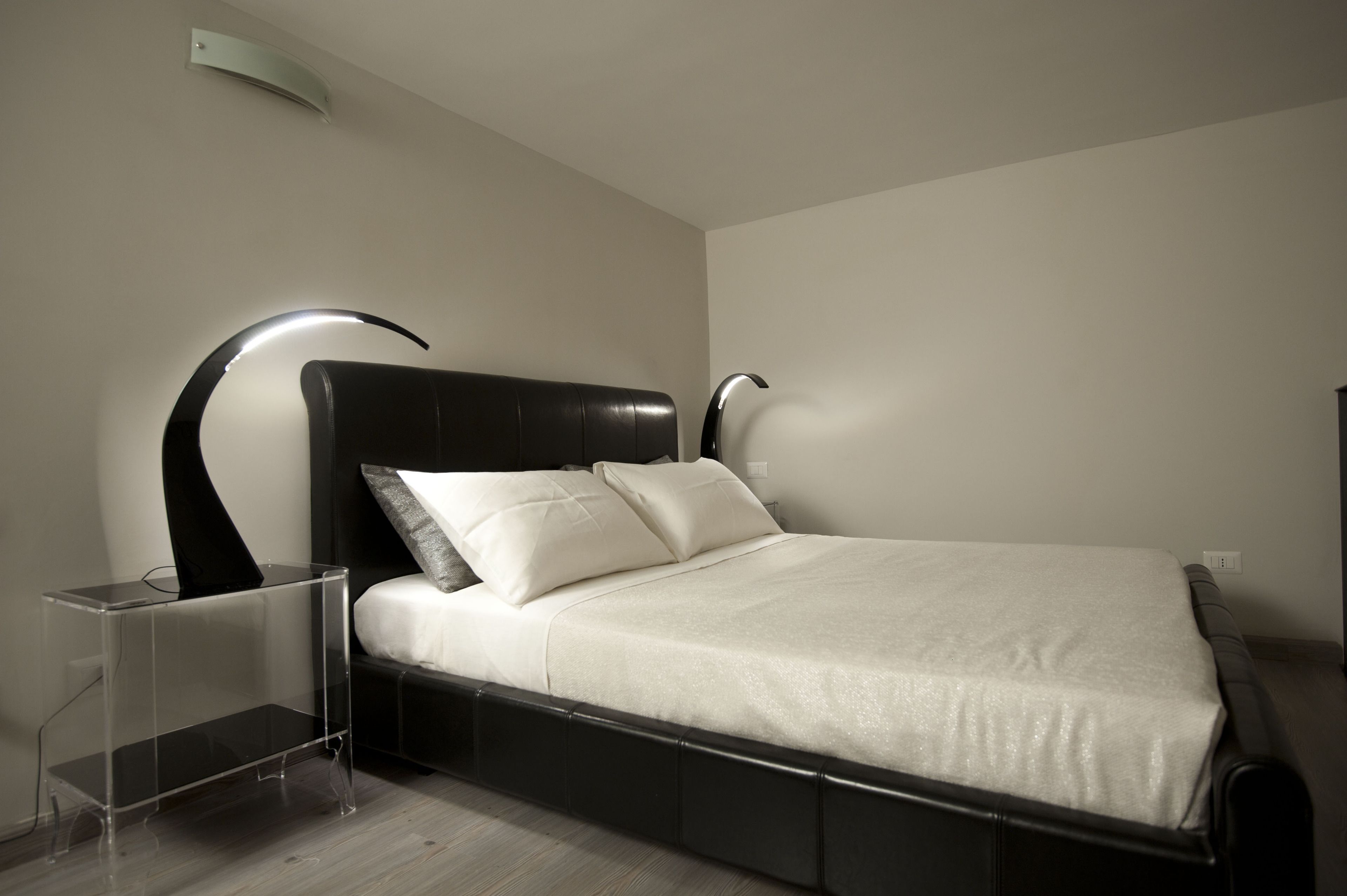 Une chambre à coucher moderne avec une tête de lit noire, une couvre-lit blanche et une table de chevet transparente.