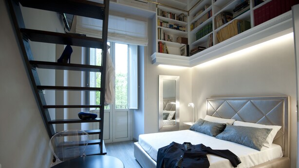 A modern bedroom with a bed, a chair, a small table, a bookshelf, and a window. - Luxury on the River (Rome)