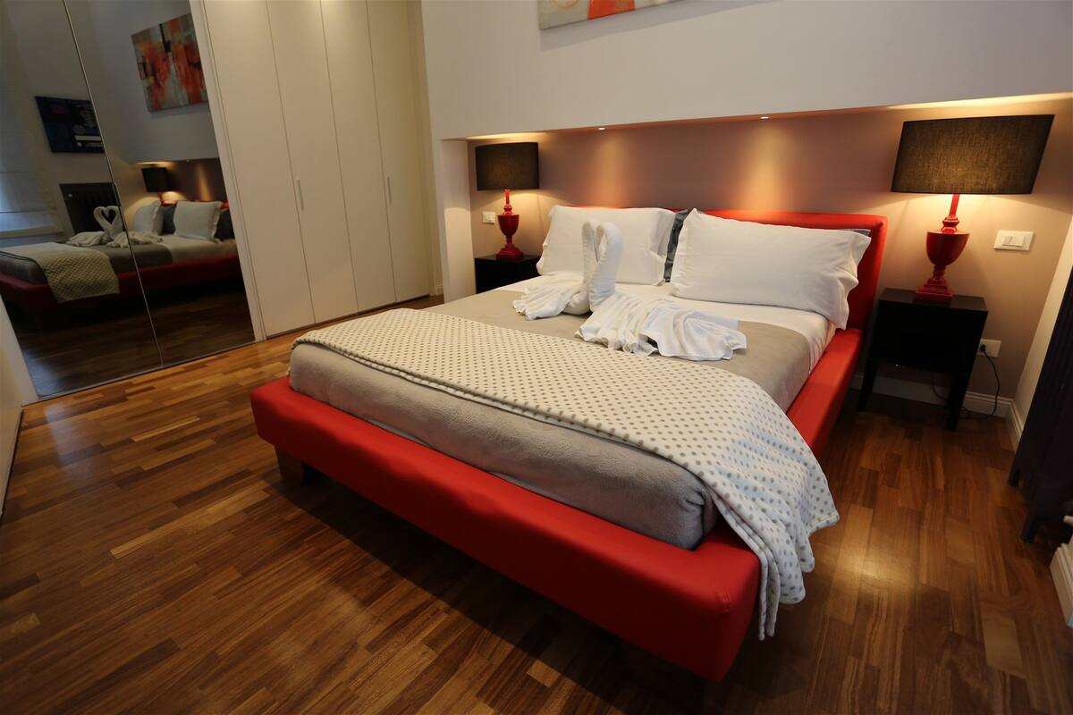 A modern bedroom with a large bed, wooden flooring, and two bedside tables with lamps.