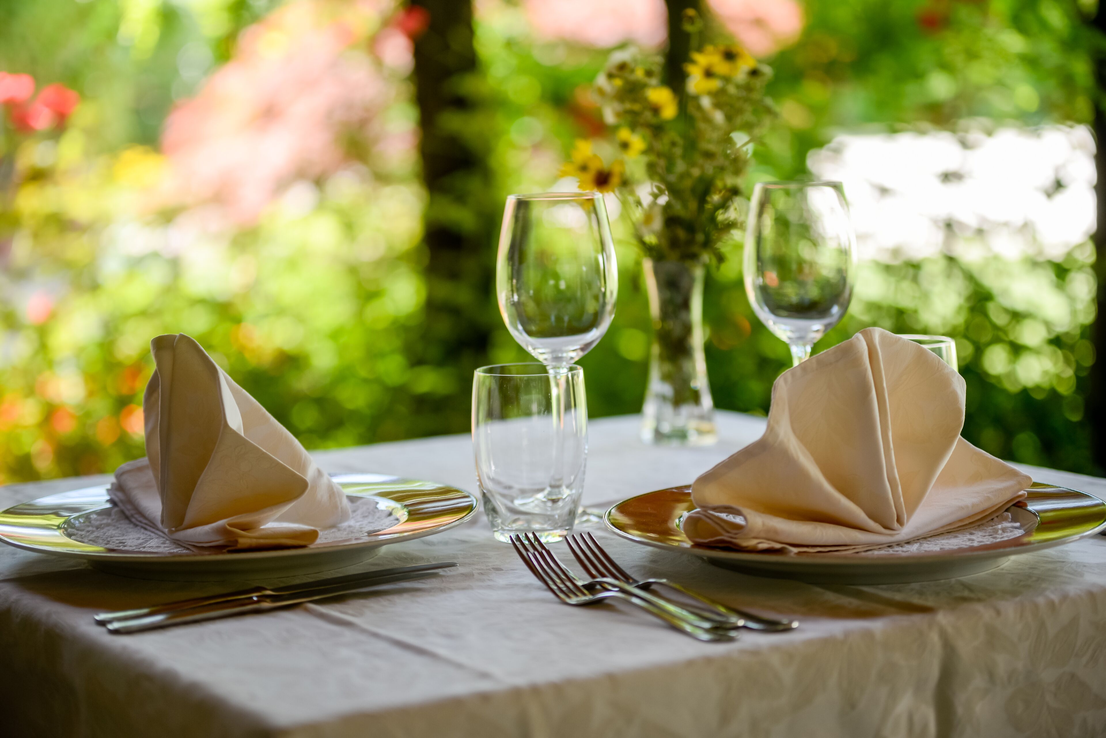 A table set with plates, cutlery, and glasses, with a vase of flowers in the background.