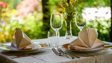 A table set with plates, cutlery, and glasses, with a vase of flowers in the background.