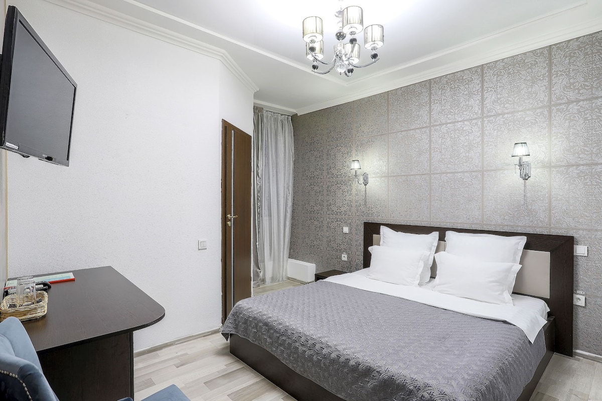 Una habitación de hotel con cama, escritorio, televisor y candelabro.