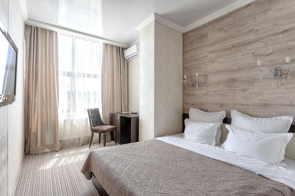 Una habitación de hotel con una cama grande, un escritorio, una silla y un ventanal con cortinas.