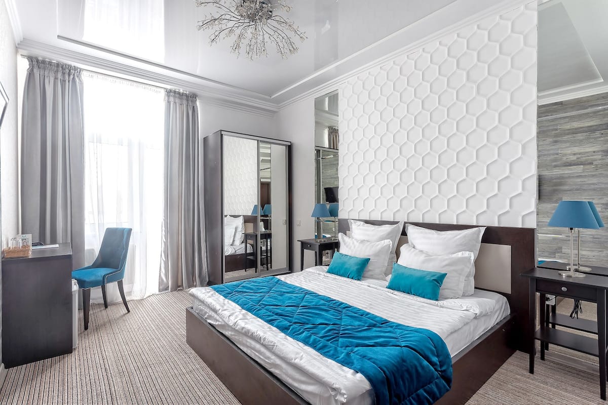 Una habitación de hotel con una cama grande, un escritorio, una silla, un armario y un espejo.