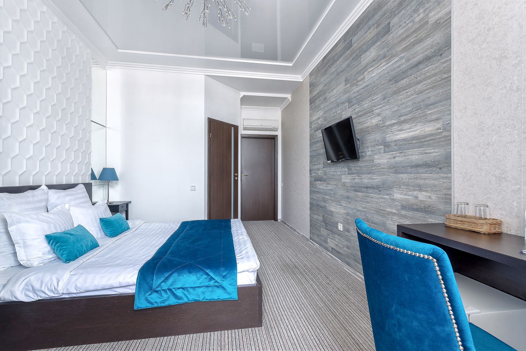 A modern hotel room with a bed, a desk, a TV, and a wall-mounted air conditioner.