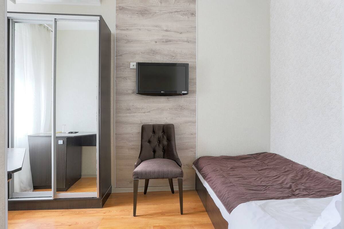 Un dormitorio con cama, una silla, un escritorio y un televisor en la pared.