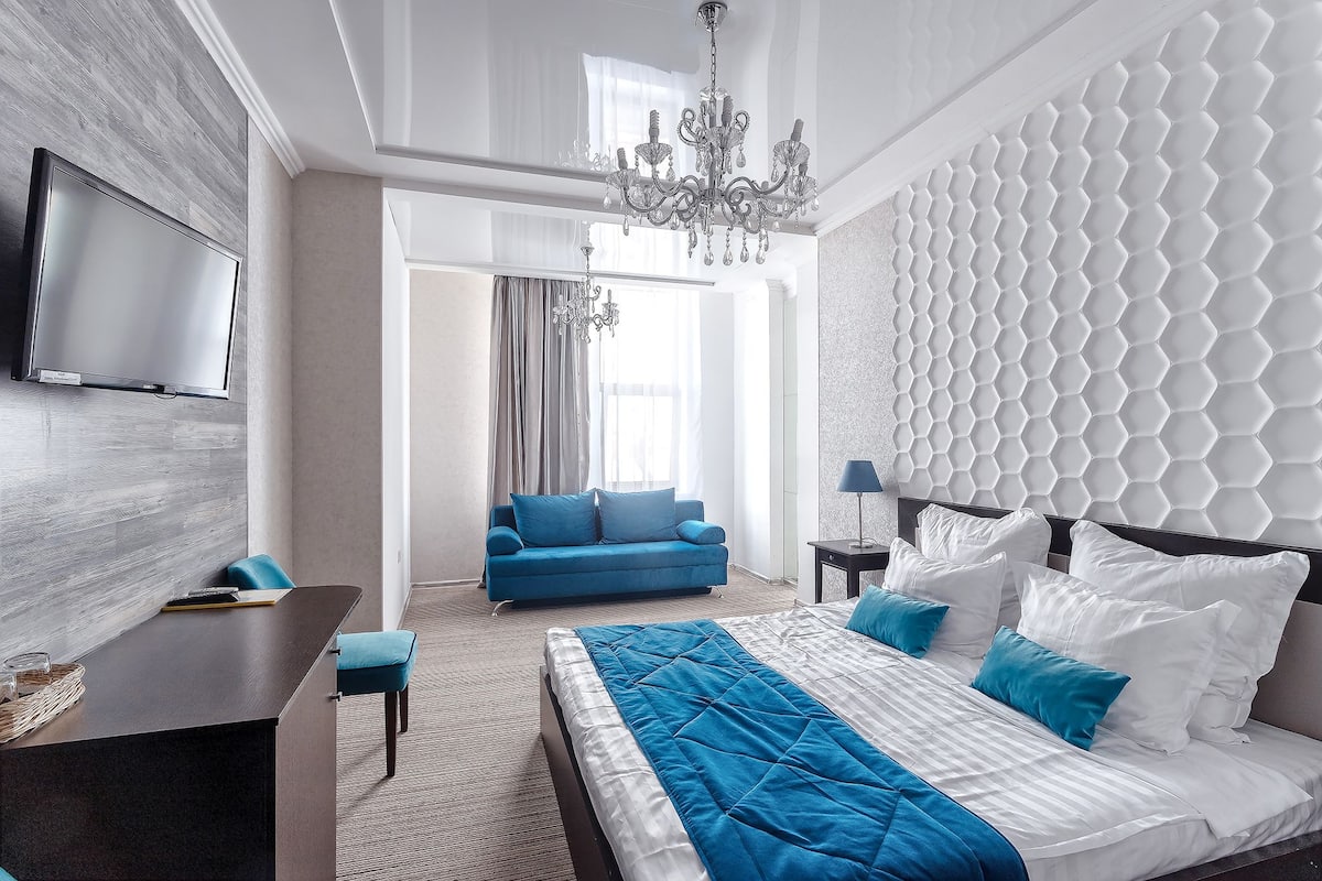 Una habitación de hotel moderna con una cama grande, un escritorio, un sofá azul y una araña.