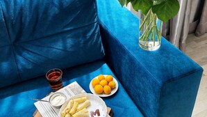 Ein blaues Sofa mit einer Schale Zitronen, einer Portion Pommes und einem Glas rotem Getränk auf einem Holzteller.