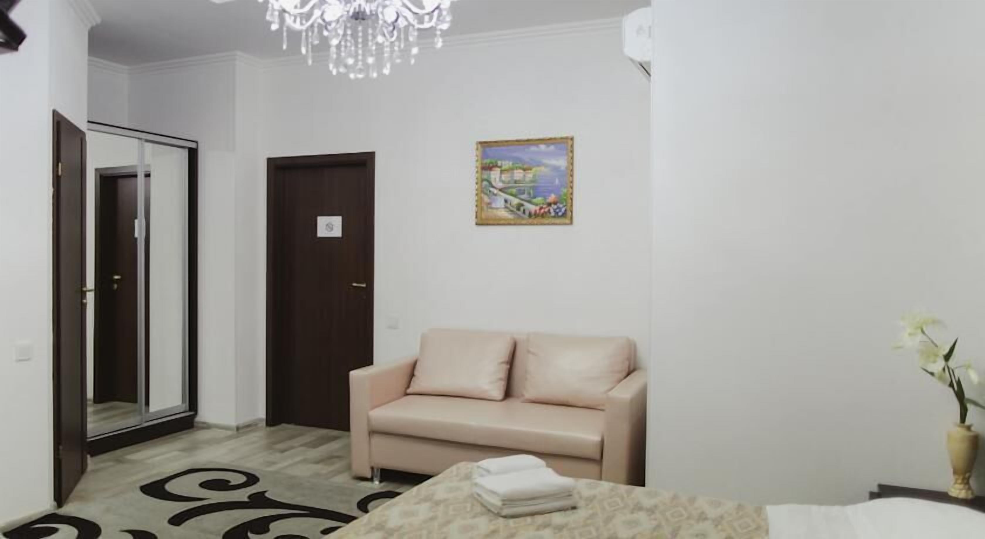 A room with a beige sofa, a small table with a folded white cloth, a painting on the wall, and a door with a sign.