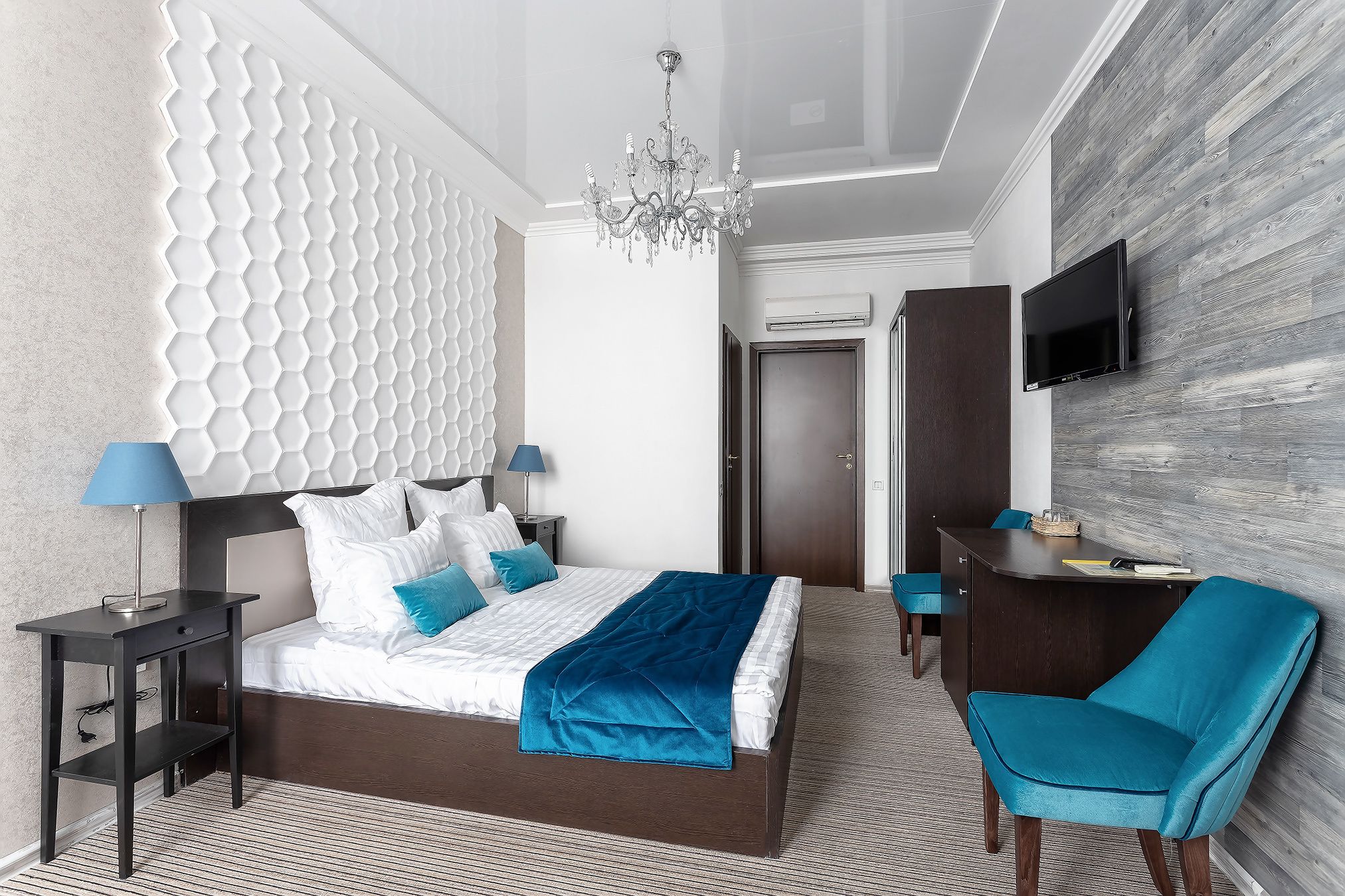 Una habitación de hotel moderna con una cama grande, un escritorio, una silla y un televisor en la pared.