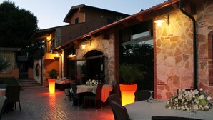 An outdoor dining area with stone walls and tables set for dining, featuring warm lighting and potted plants. - Borgo dei Vigneti (Agrigento)