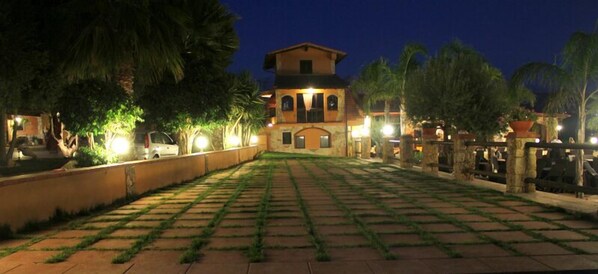 A courtyard with a stone pathway leading to a building with arched windows and a balcony. - Borgo dei Vigneti (Agrigento)