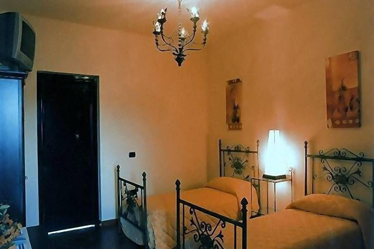 A bedroom with a bed, bedside tables, a chandelier, and a door.