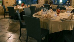 A restaurant with stone walls and large arched windows overlooking a scenic view. Tables are set with white tablecloths, napkins, and wine glasses. - Borgo dei Vigneti (Agrigento)
