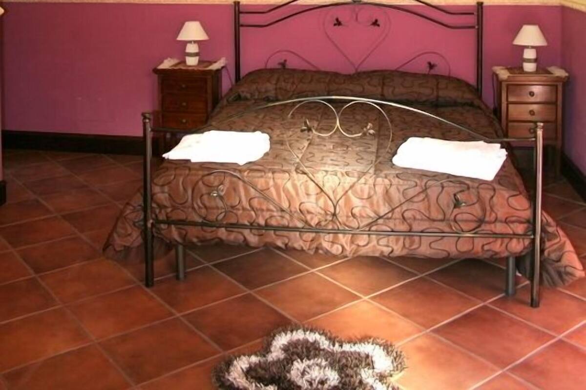 A bedroom with a bed, two bedside tables, a chandelier, and a framed picture on the wall.