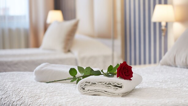 A neatly made bed with a folded towel and a rose, a bedside lamp, and a striped wall in a hotel room.