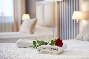 A neatly made bed with a folded towel and a rose, a bedside lamp, and a striped wall in a hotel room. - Willa Labelle (Zakopane)