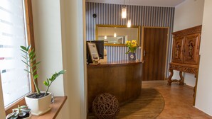 A reception area with a wooden reception desk, a mirror, a vase with yellow flowers, and a wicker ball.