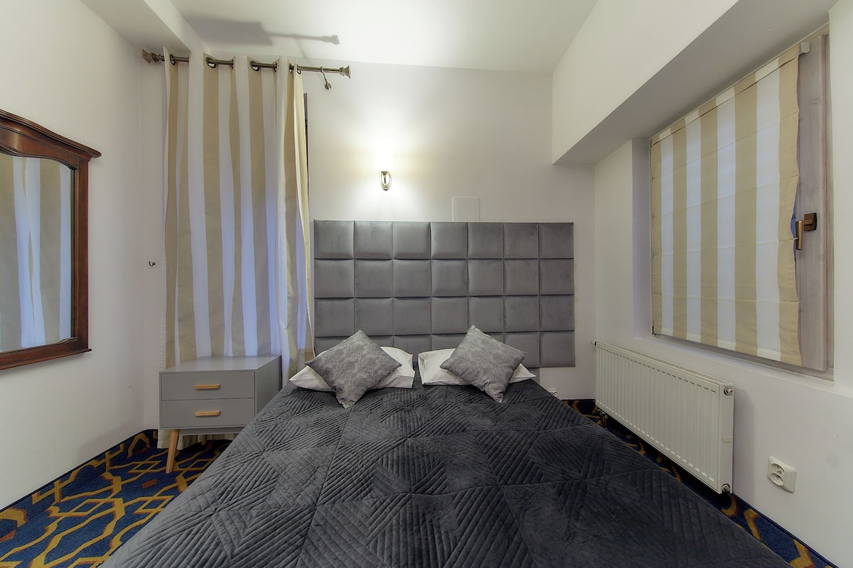 A bedroom with a large bed, a headboard, a nightstand, a mirror, a radiator, and striped curtains.