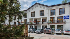A white building with multiple balconies, a stone wall, and a paved driveway.
