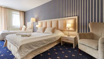 Ein Hotelzimmer mit zwei Betten, einem großen Kopfteil, Nachttischlampen, einem Sessel und einem gemusterten Teppich.