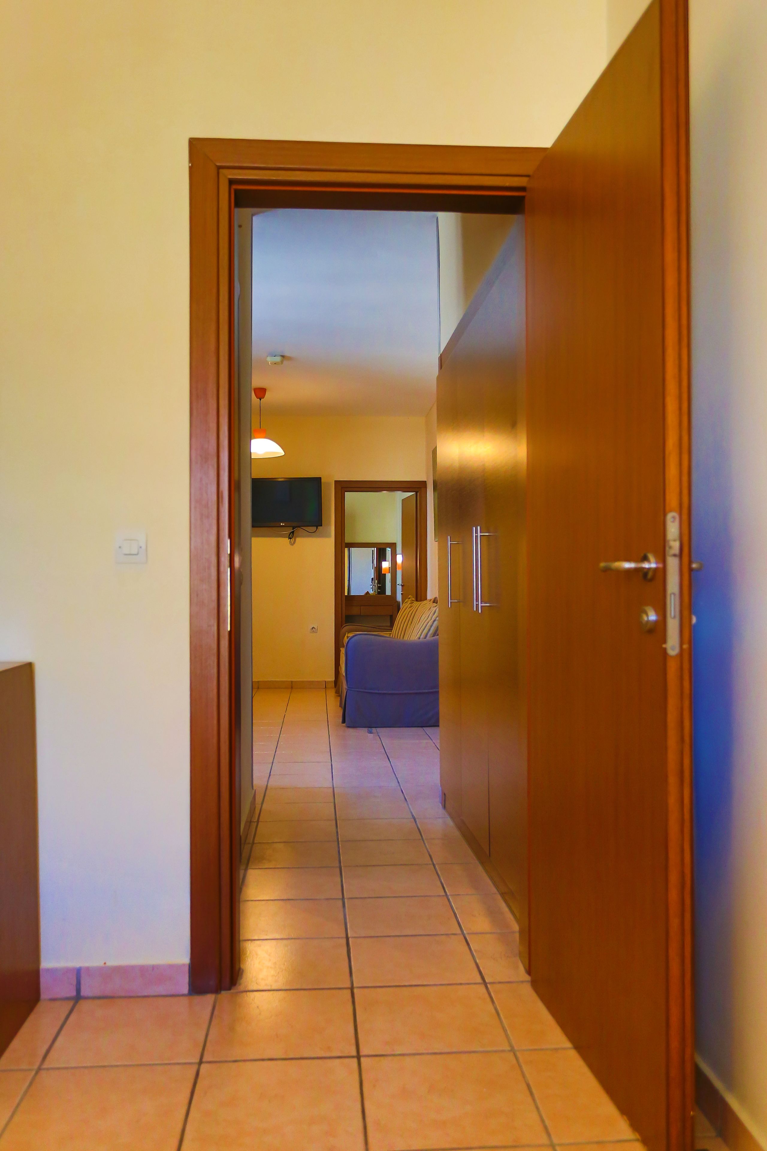A hallway with a wooden door, a television mounted on the wall, and a couch in the background.
