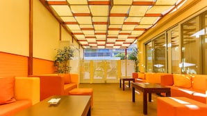 A modern indoor seating area with orange sofas and wooden tables, featuring a glass partition and potted plants. - Rodian Gallery Hotel Apartments (Rhodes)