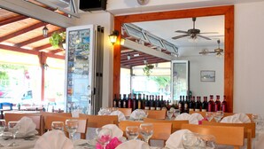 A restaurant with multiple tables set for dining, a wine rack with various bottles, and a view of the street outside. - Rodian Gallery Hotel Apartments (Rhodes)
