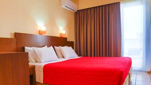 A hotel room with a bed, a nightstand, an air conditioning unit, and a window with curtains. - Rodian Gallery Hotel Apartments (Rhodes)