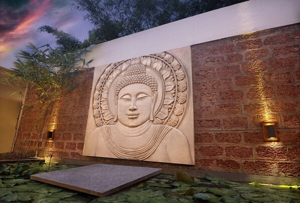 A stone Buddha sculpture on a brick wall with two wall-mounted lights.