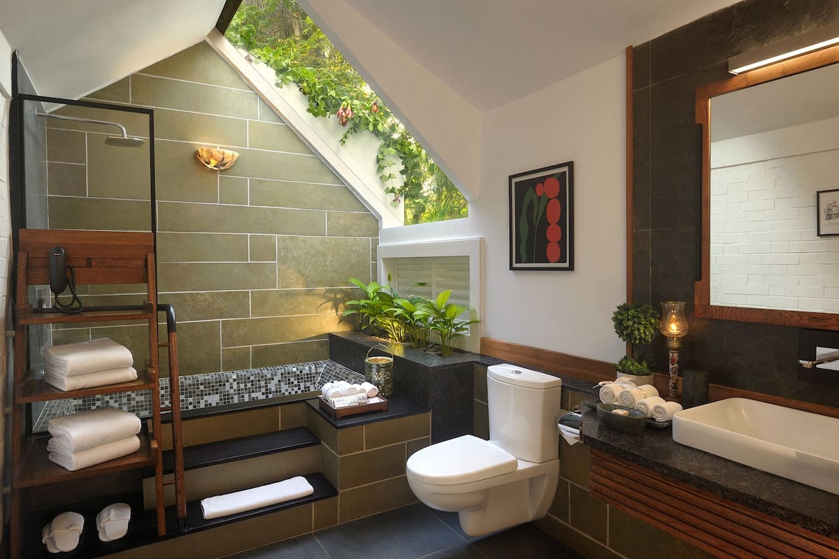 A modern bathroom with a glass shower enclosure, a toilet, a sink, and a wooden shelf with towels.