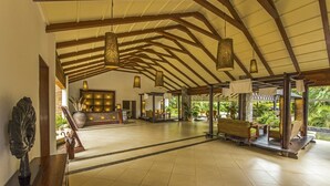 A spacious lobby with a high ceiling, wooden beams, and hanging lanterns. There are seating areas with cushions and a reception desk with a lit display. - The Windflower Resorts & Spa (Somvarpet)