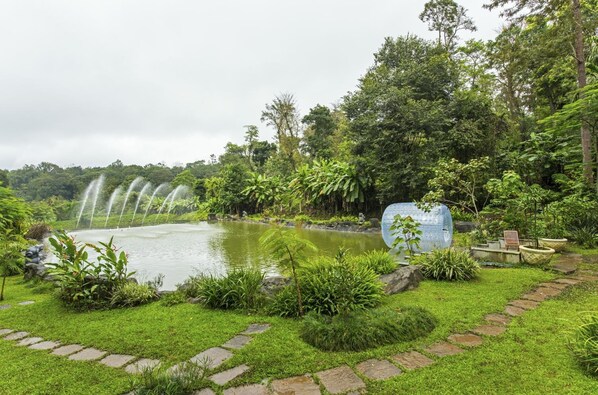 Un jardín con un estanque, un sendero de piedra y una gran escultura transparente.