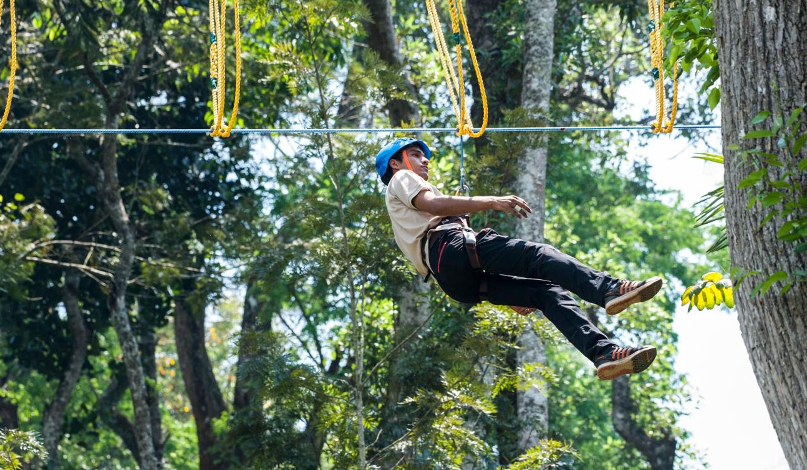 A person zip-lining through a forested area with trees and ropes.