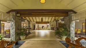 A spacious lobby with a high ceiling, stone pillars, and a central seating area with a view of the back of the room. - The Windflower Resorts & Spa (Somvarpet)