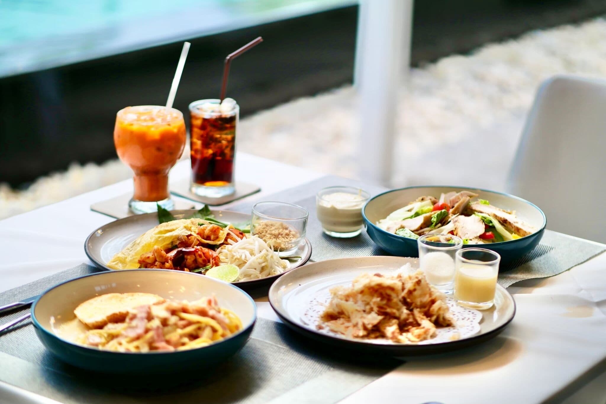 Una mesa dispuesta con diferentes platos, bebidas y acompañamientos, indicando una experiencia culinaria.
