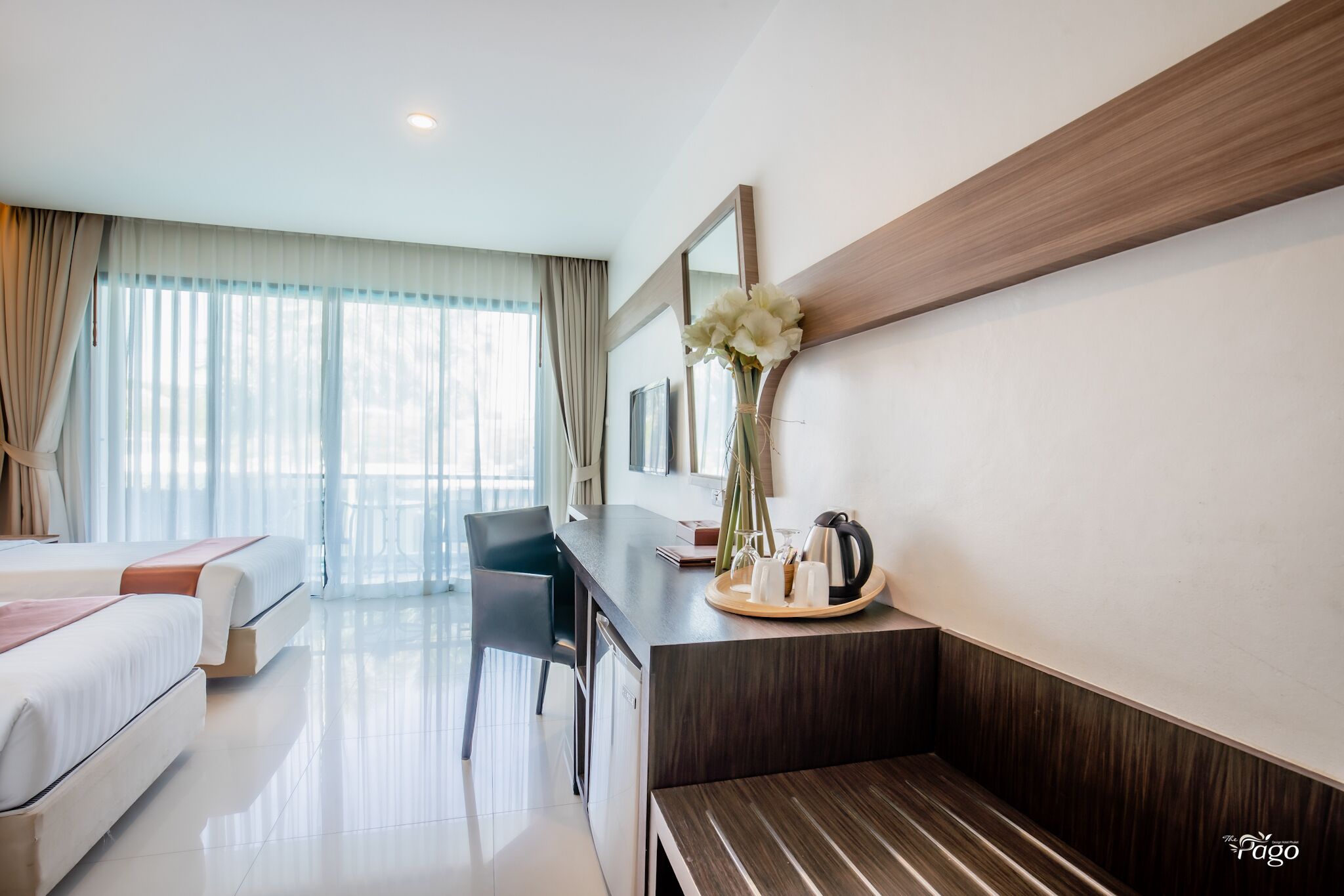 A modern hotel room with a bed, a desk with a vase of flowers, a chair, and a large window with curtains.