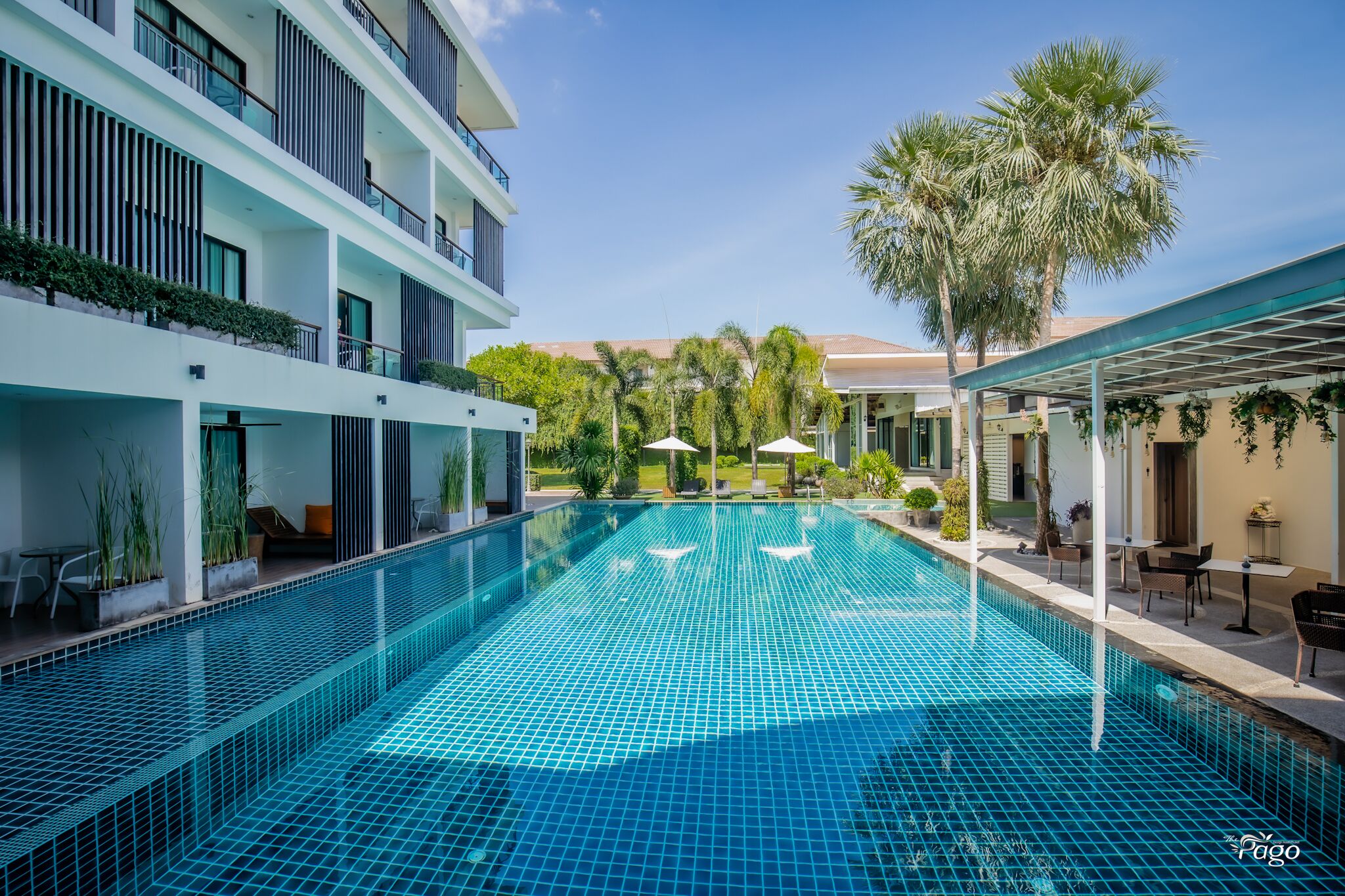 A swimming pool with a tiled deck, surrounded by a modern building with balconies and outdoor seating.