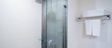 Una ducha moderna con puerta de vidrio, cabezal de ducha de vidrio y un perchero con toallas dobladas.